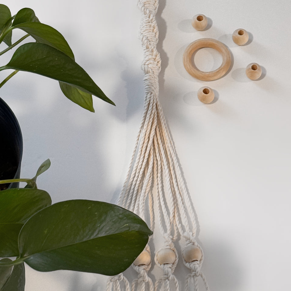 Macrame Plant hanger lying over white table with wooden rings and plant leaves over it